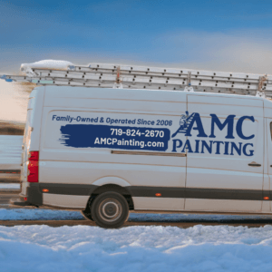 An AMC Painting truck is parked outside on a snowy day.